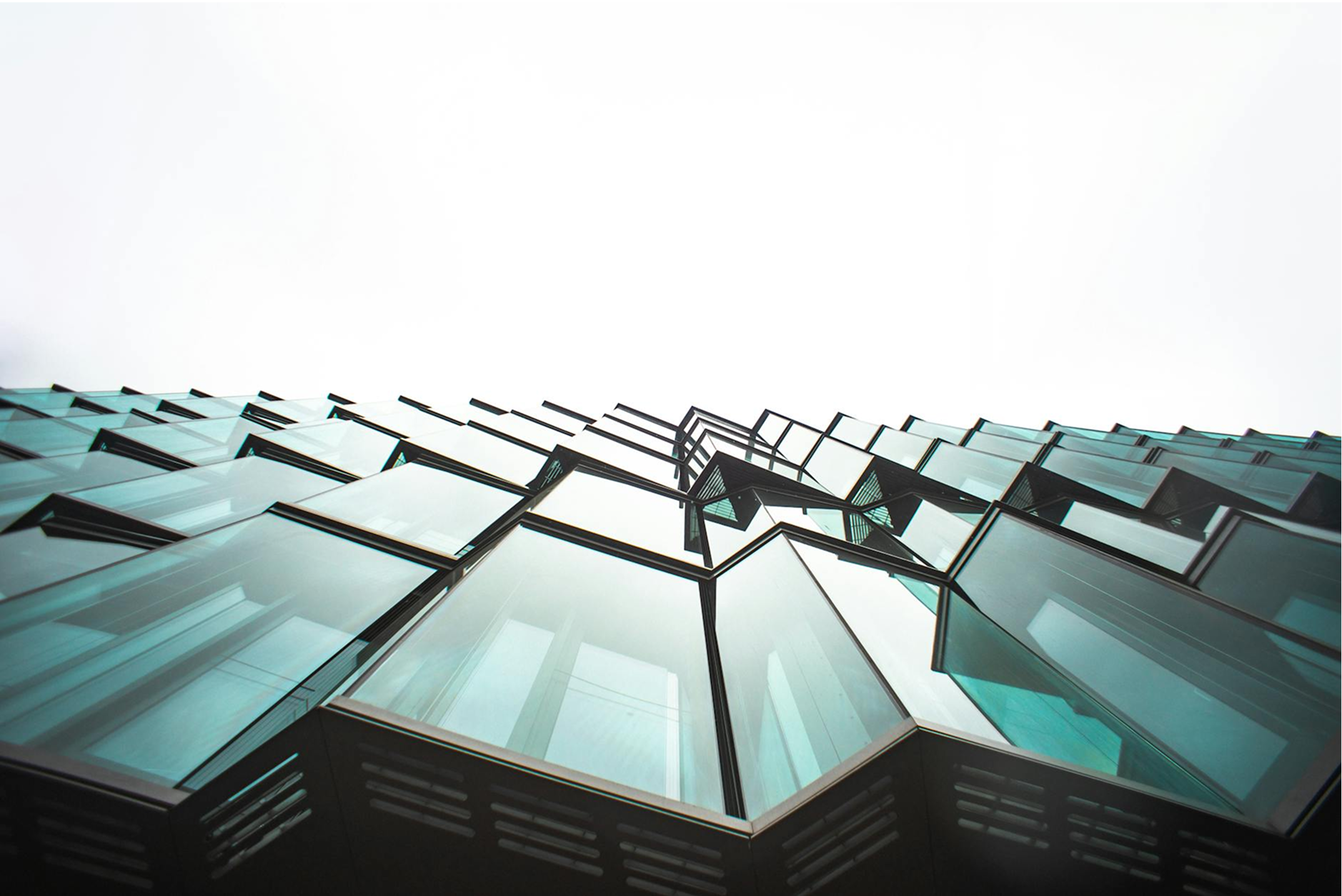 A glass-walled office building photographed from below against a gray sky.